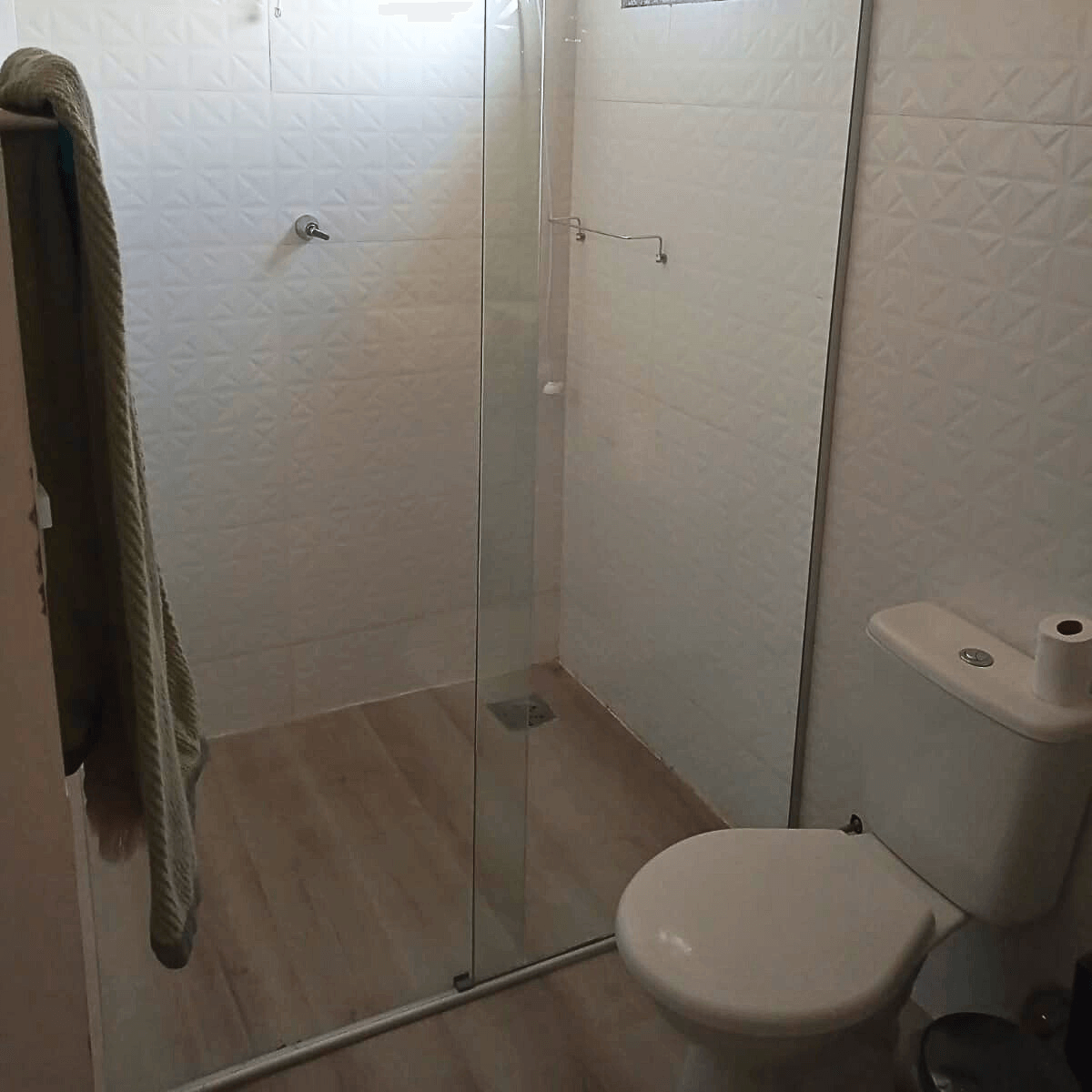 Banheiro compacto com instalação de piso resistente à umidade e box de vidro.