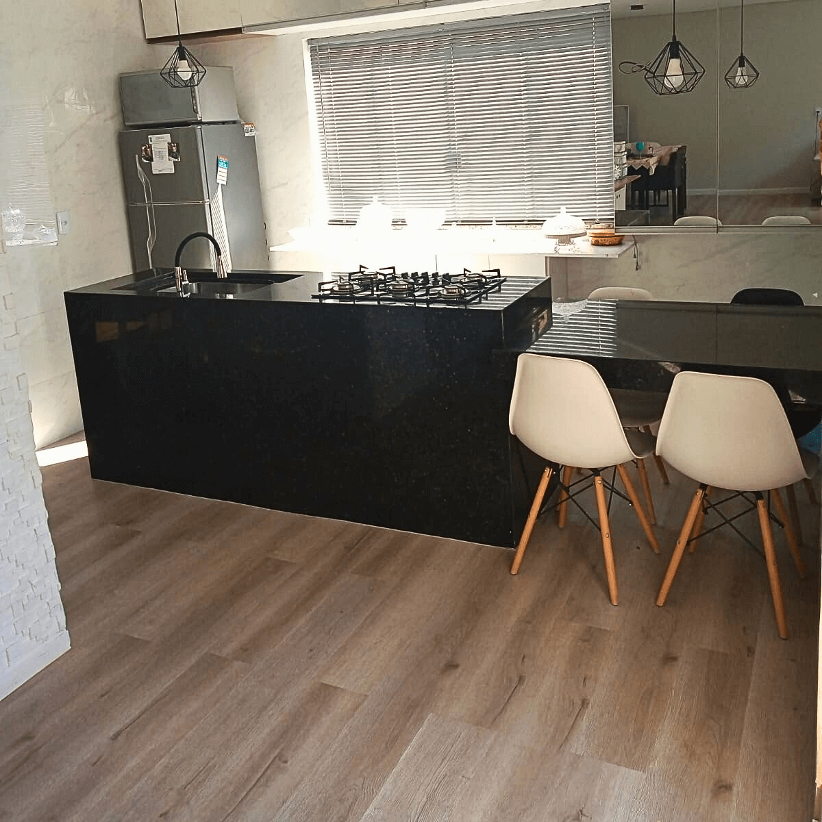Cozinha integrada com sala de jantar, ilha preta e piso vinílico contínuo para ampliar o ambiente.