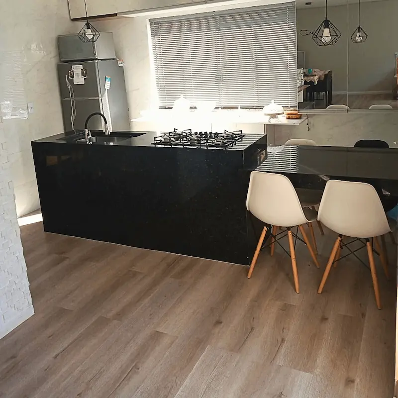 Cozinha integrada com sala de jantar, ilha preta e piso vinílico contínuo para ampliar o ambiente.
