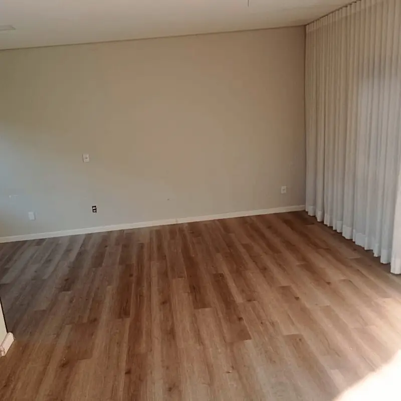 Sala residencial vazia após instalação de piso laminado cor madeira natural e rodapés brancos.