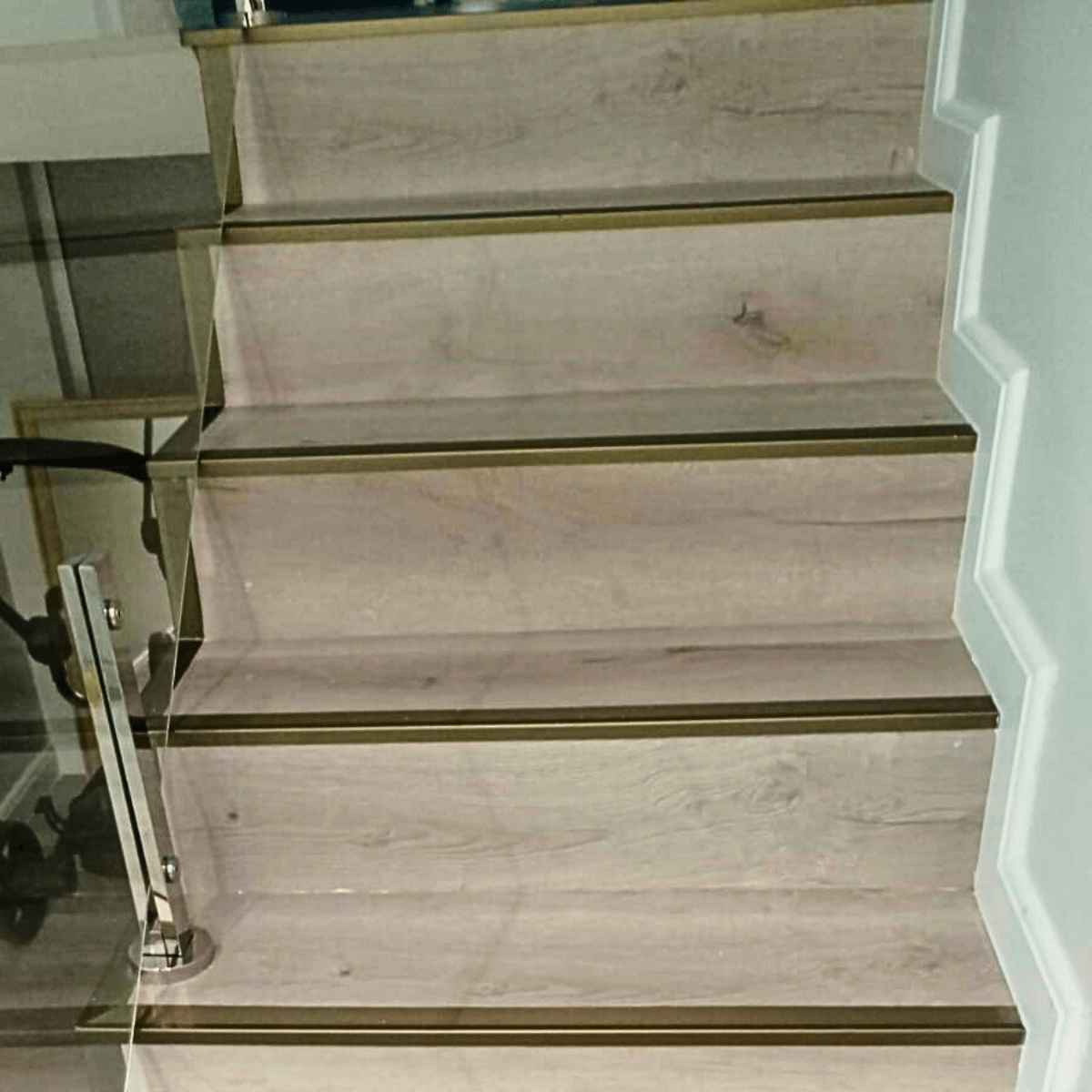 Detalhe dos degraus da escada com revestimento amadeirado e perfil de acabamento metálico antiderrapante.