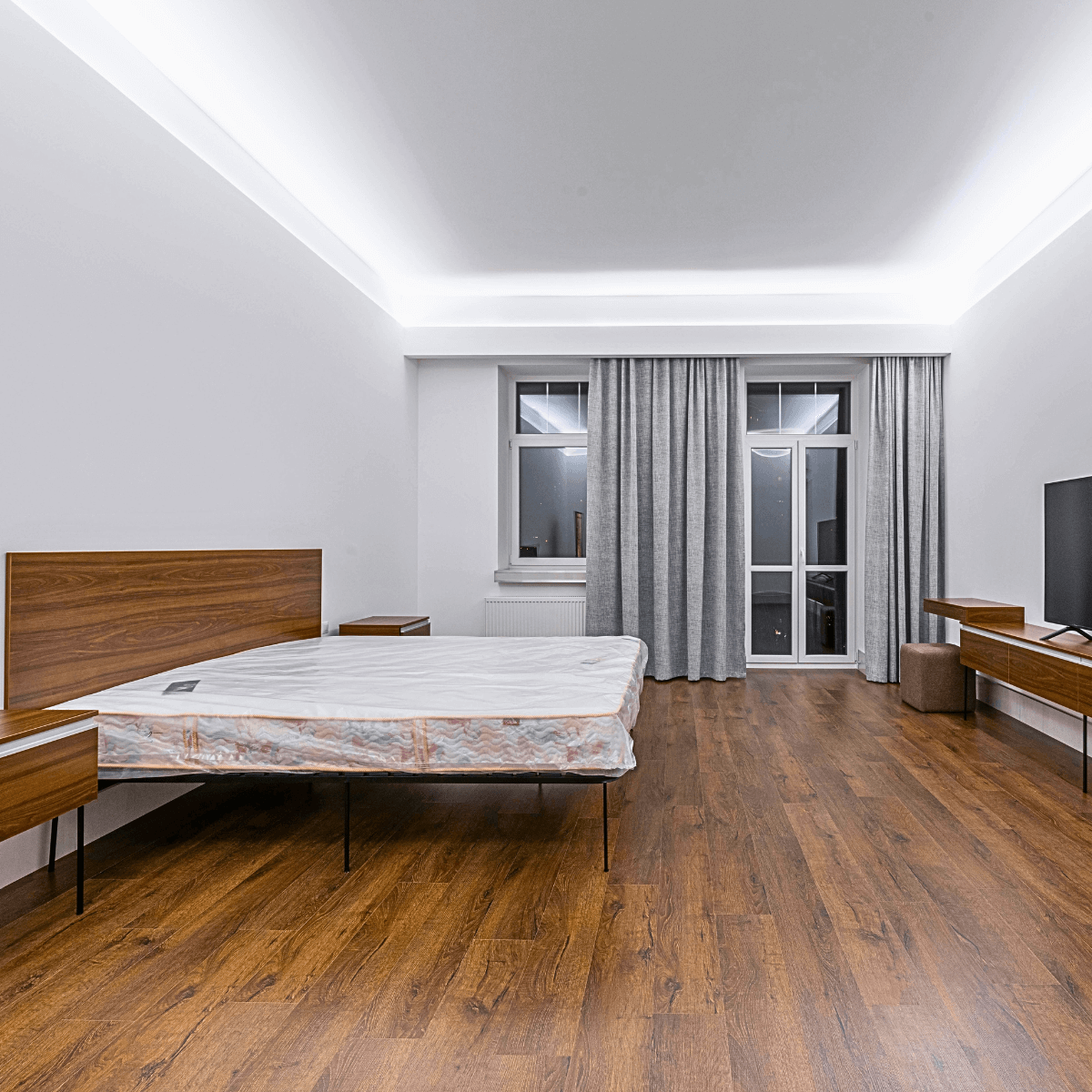 Quarto de casal decorado com iluminação em sanca e piso laminado confortável e térmico.